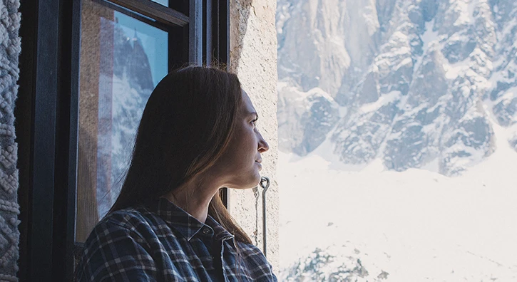 Une femme qui contemple à sa fenêtre la vue d'un paysage montagneux et enneigé