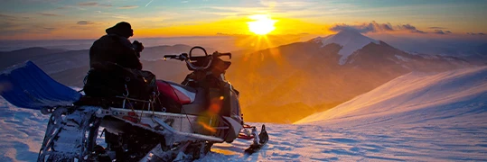Un homme admire un coucher de soleil sur sa motoneige