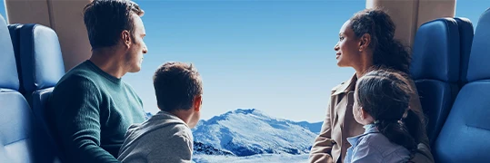 Une famille dans un train qui contemple la vue d'un paysage de montagnes enneigées