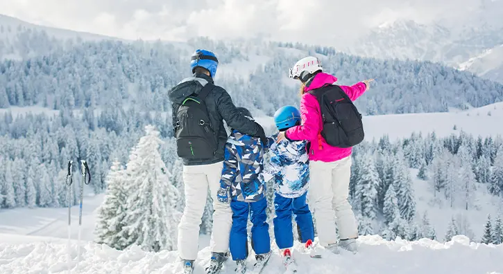 Une famille contemple le paysage face à une forêt de sapins enneigés