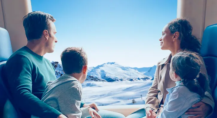 Une famille dans un train qui admire la vue d'un paysage de montagnes enneigées